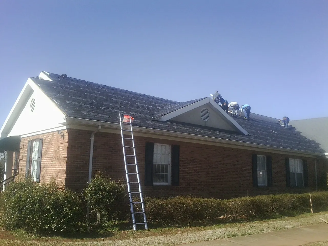 Crew tearing shingles off a brick ranch roof with a ladder set — Emergency Roof Repair work by our crew in Mulga