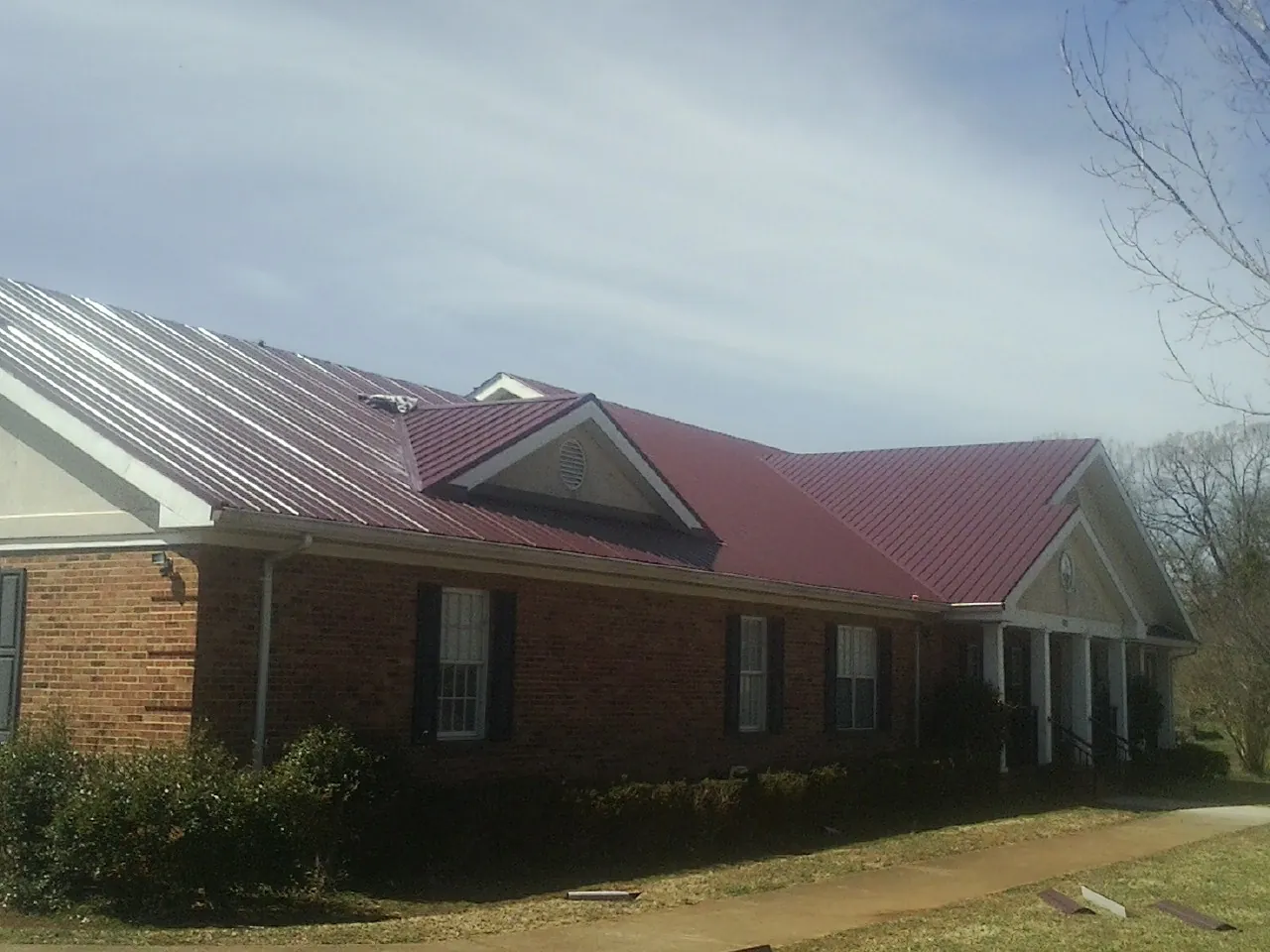 Red metal roof with gabled entries on a long brick building, from a Hail Damage Roof Repair job in Mulga