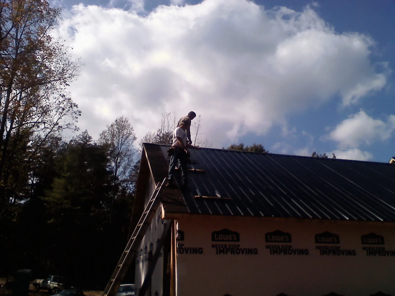 Roofer fastening dark metal panels high against a cloudy sky, from a Roof Inspection job in Mulga