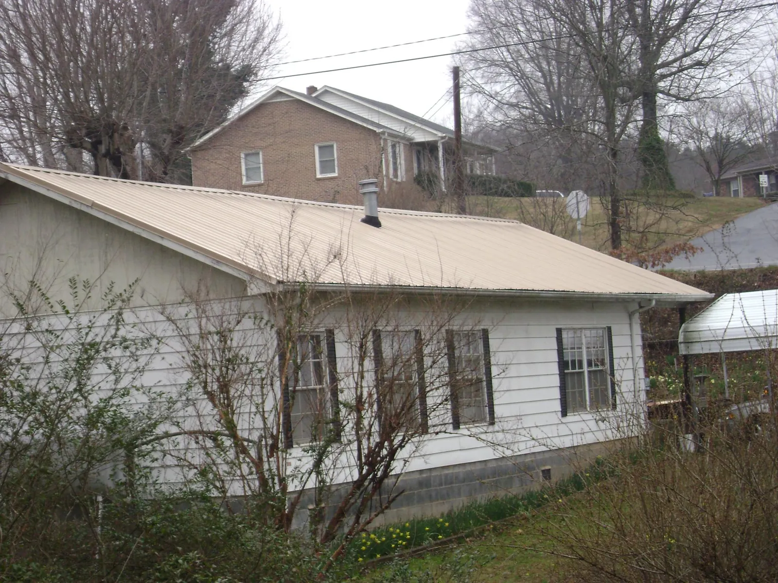 Tan metal roof on a white sided house set into a hillside — Commercial Roofing by Roofing Brothers in Mulga
