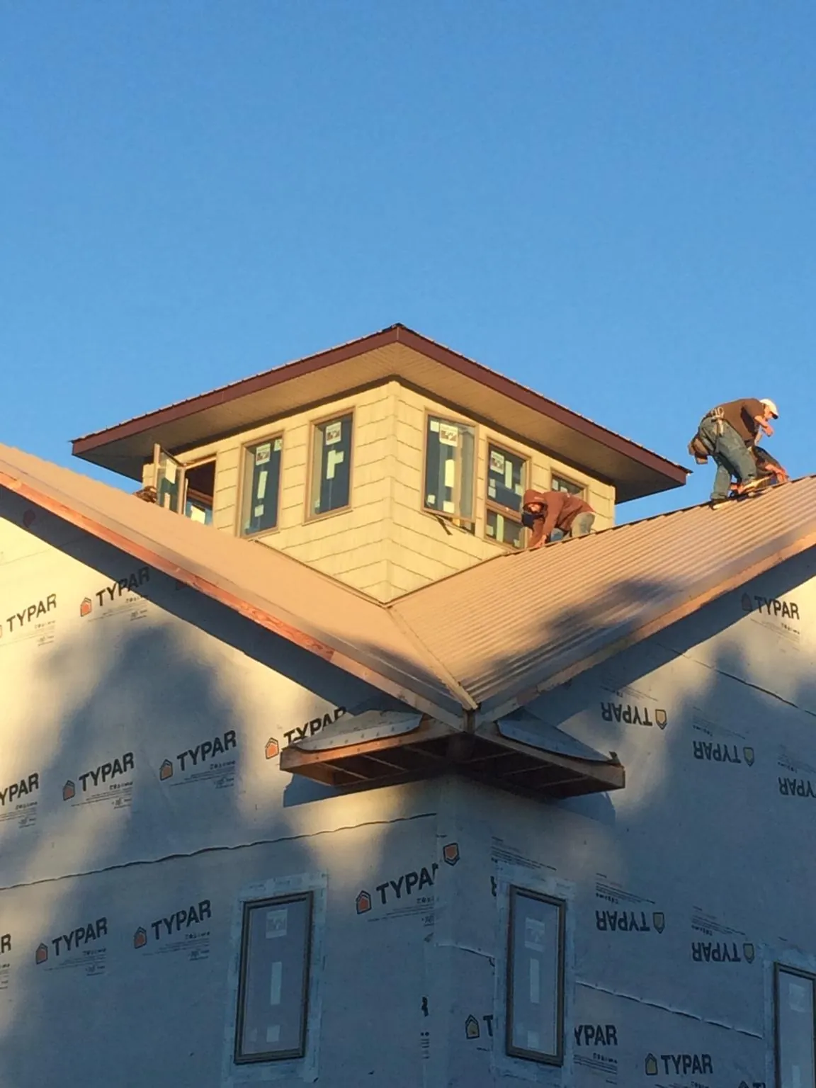 Roofers working around a rooftop cupola on a new metal roof at sunset — Roof Waterproofing in Mulga by Roofing Brothers